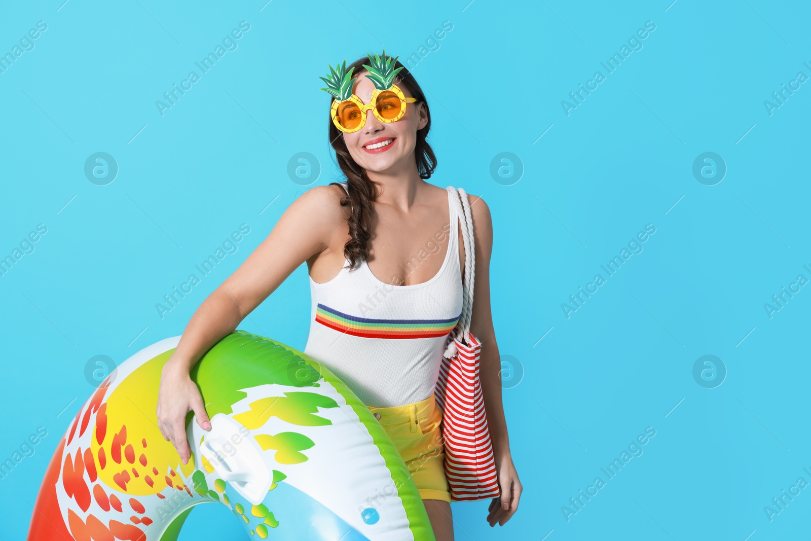 Photo of Beautiful woman wearing swimsuit and funny sunglasses with inflatable ring on light blue background