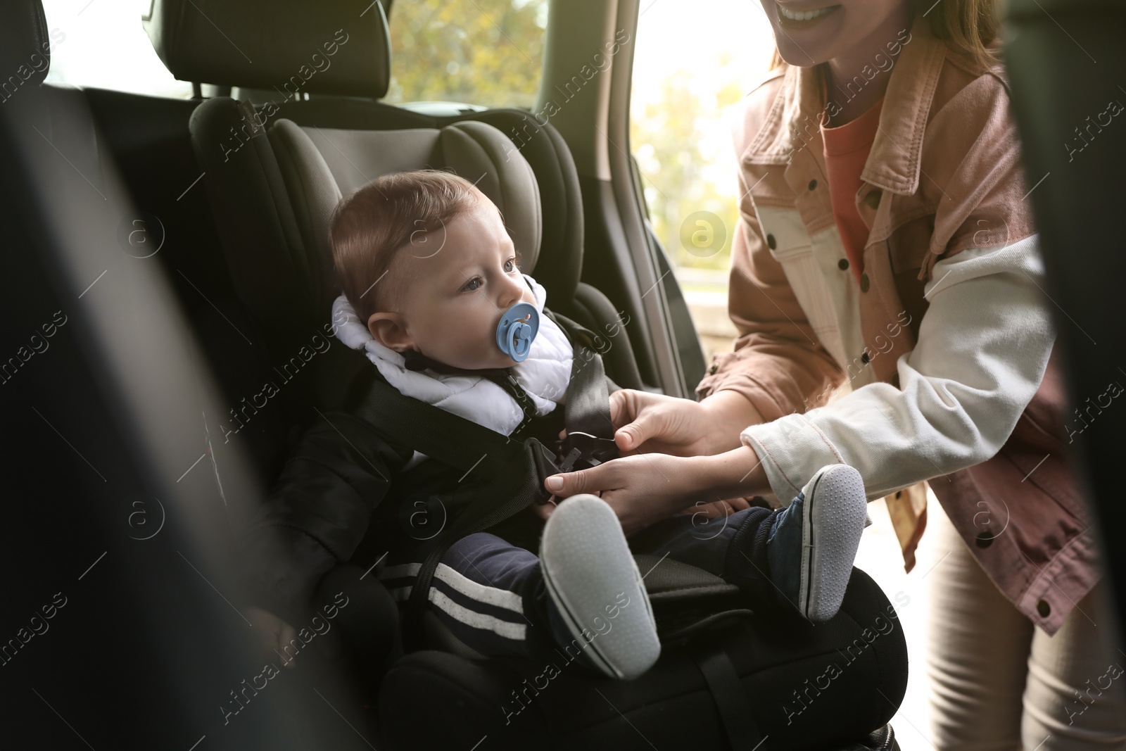 Photo of Smiling mother fastening her baby in car seat, closeup