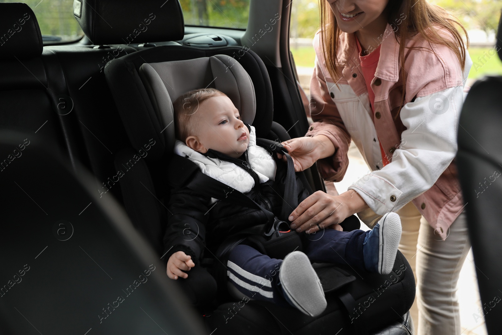 Photo of Smiling mother fastening her baby in car seat, closeup