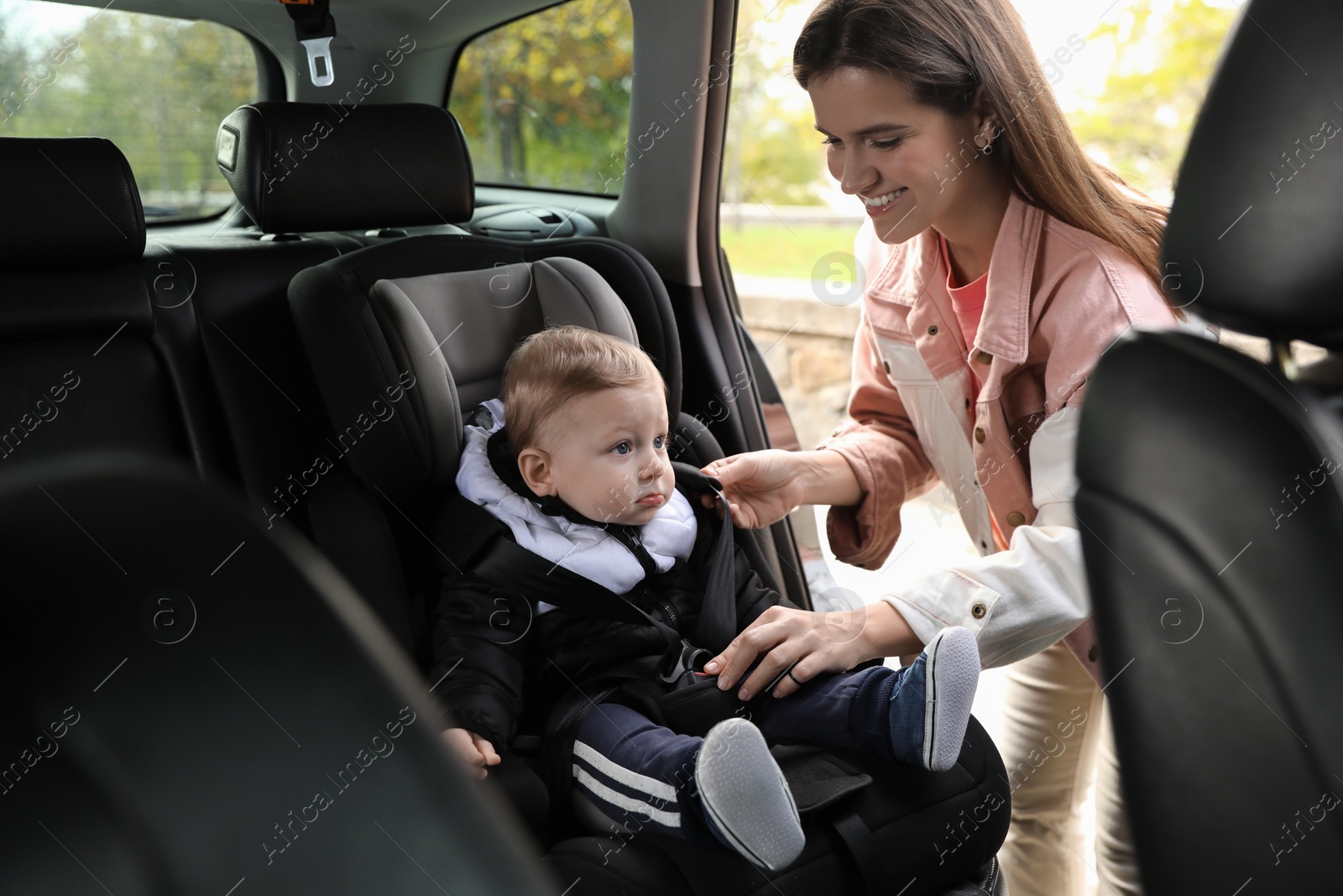 Photo of Smiling mother fastening her baby in car seat