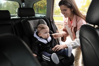 Smiling mother fastening her baby in car seat