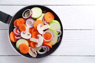 Photo of Frying pan with mix of fresh vegetables and mushrooms on white wooden table, top view