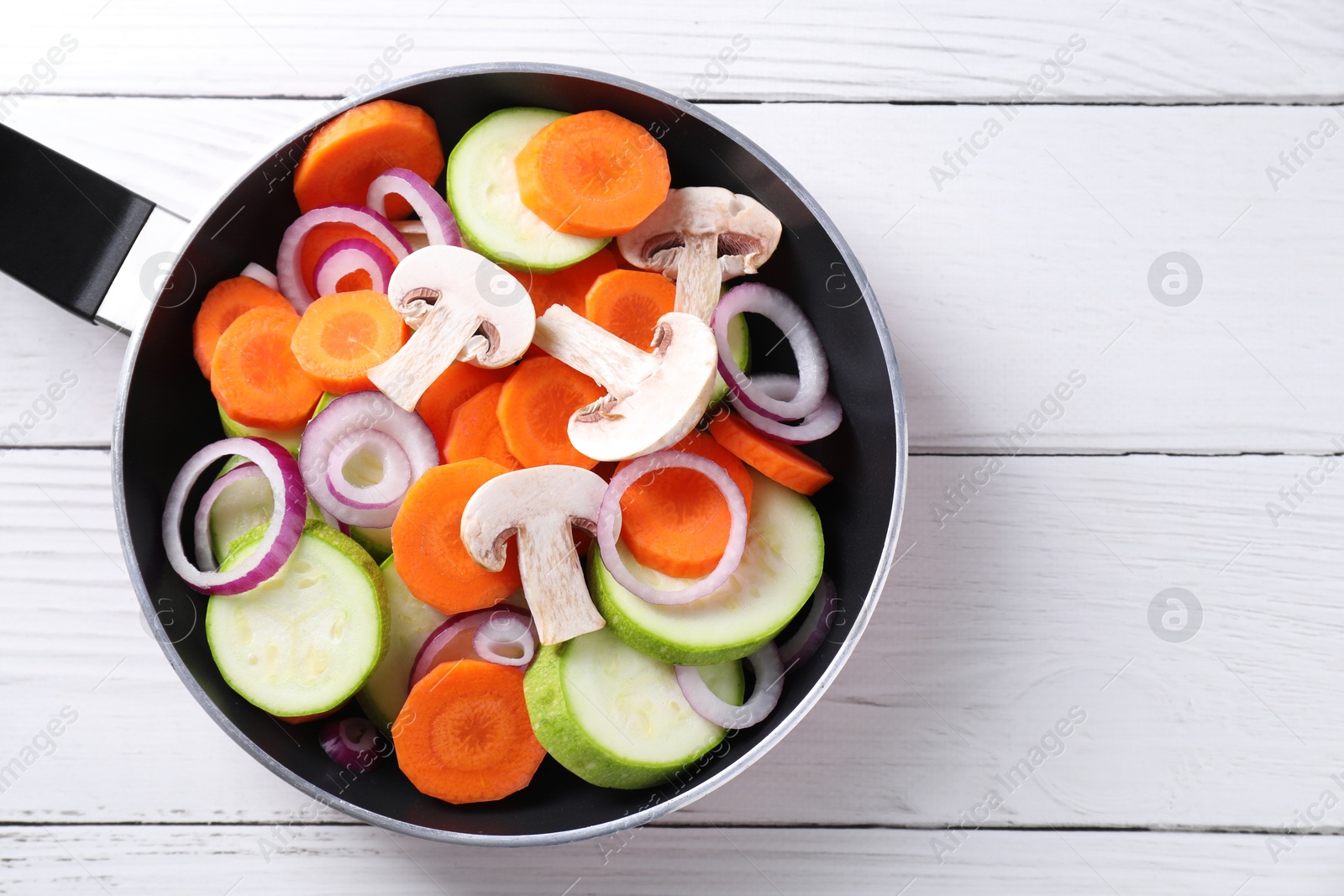 Photo of Frying pan with mix of fresh vegetables and mushrooms on white wooden table, top view. Space for text