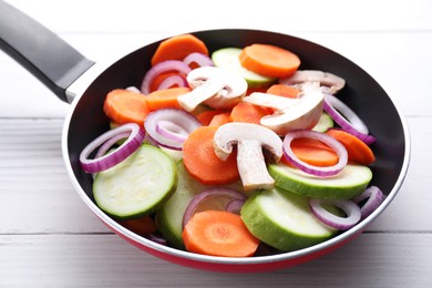 Photo of Frying pan with mix of fresh vegetables and mushrooms on white wooden table, closeup