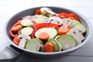 Photo of Frying pan with mix of fresh vegetables and mushrooms on white wooden table, closeup