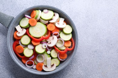 Photo of Frying pan with mix of fresh vegetables and mushrooms on grey table, top view. Space for text