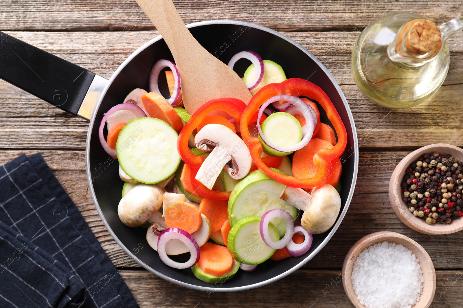 Photo of Frying pan with mix of fresh vegetables, mushrooms and spices on wooden table, flat lay