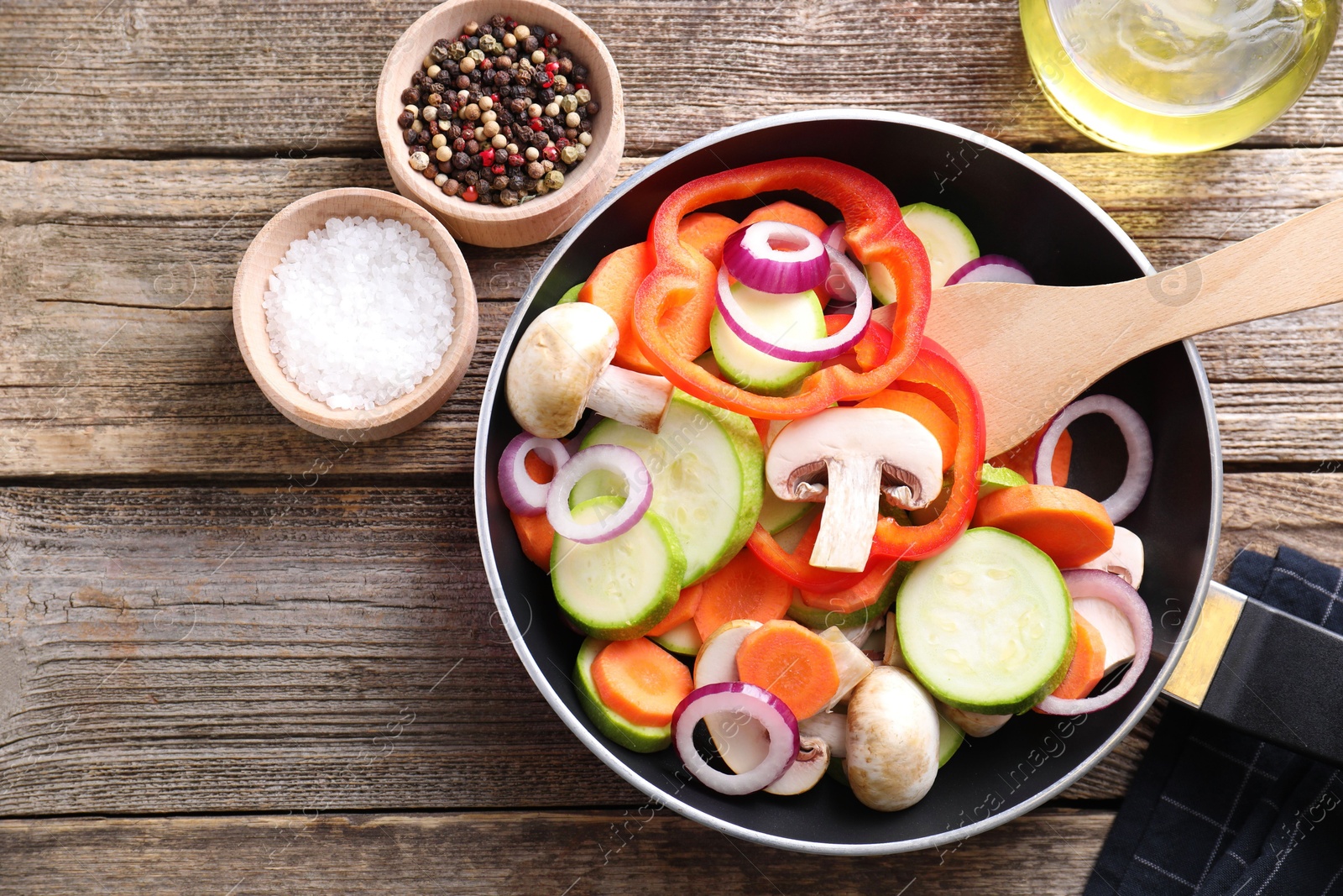 Photo of Frying pan with mix of fresh vegetables, mushrooms and spices on wooden table, flat lay