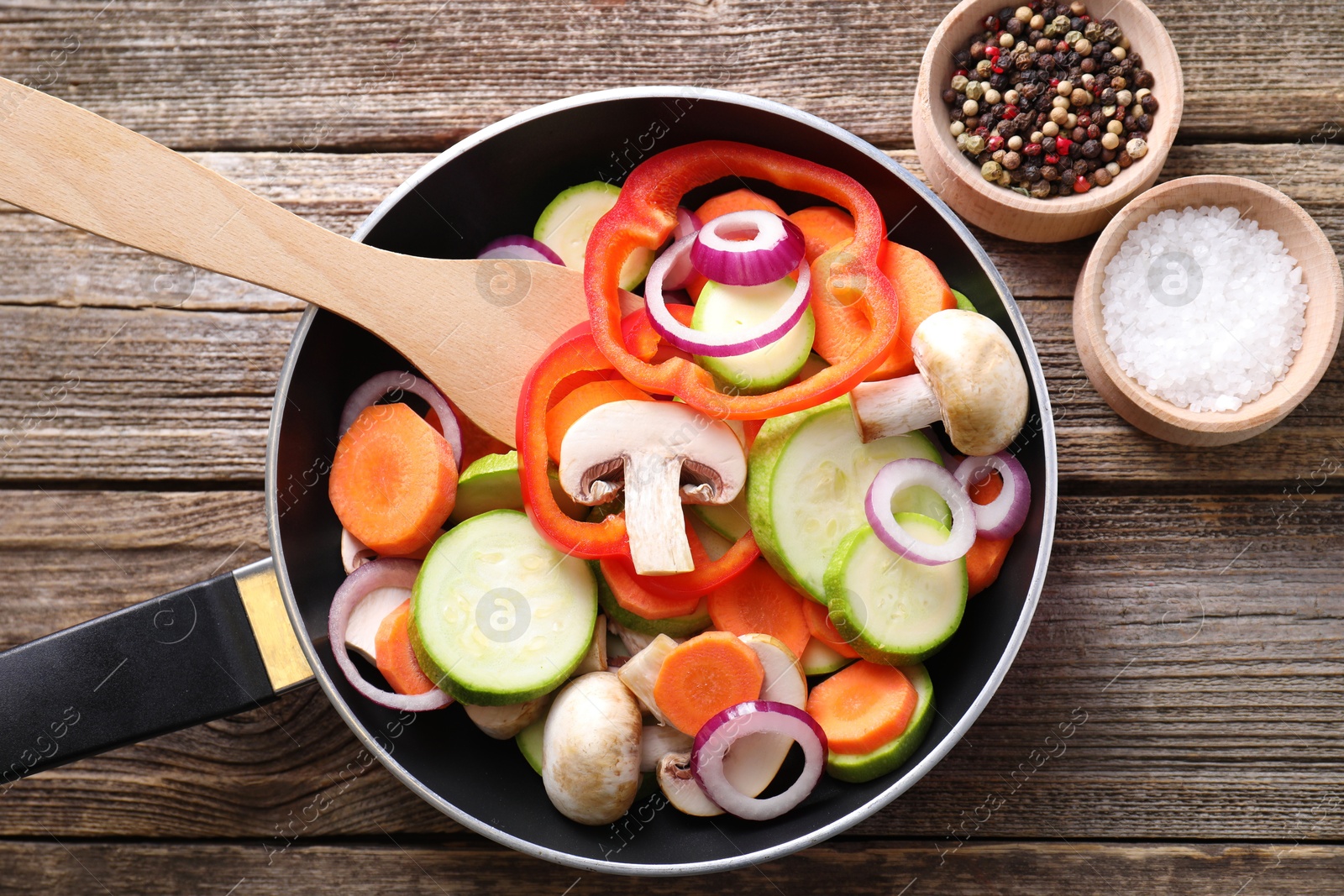 Photo of Frying pan with mix of fresh vegetables, mushrooms and spices on wooden table, flat lay