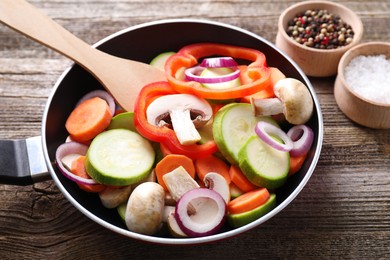 Photo of Frying pan with mix of fresh vegetables, mushrooms and spices on wooden table, closeup