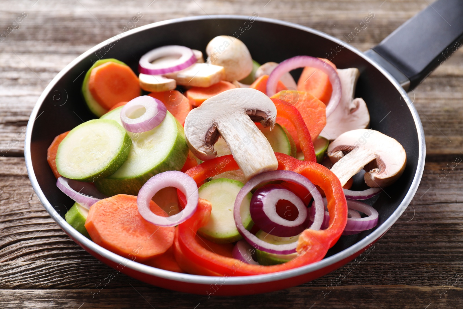 Photo of Frying pan with mix of fresh vegetables and mushrooms on wooden table, closeup