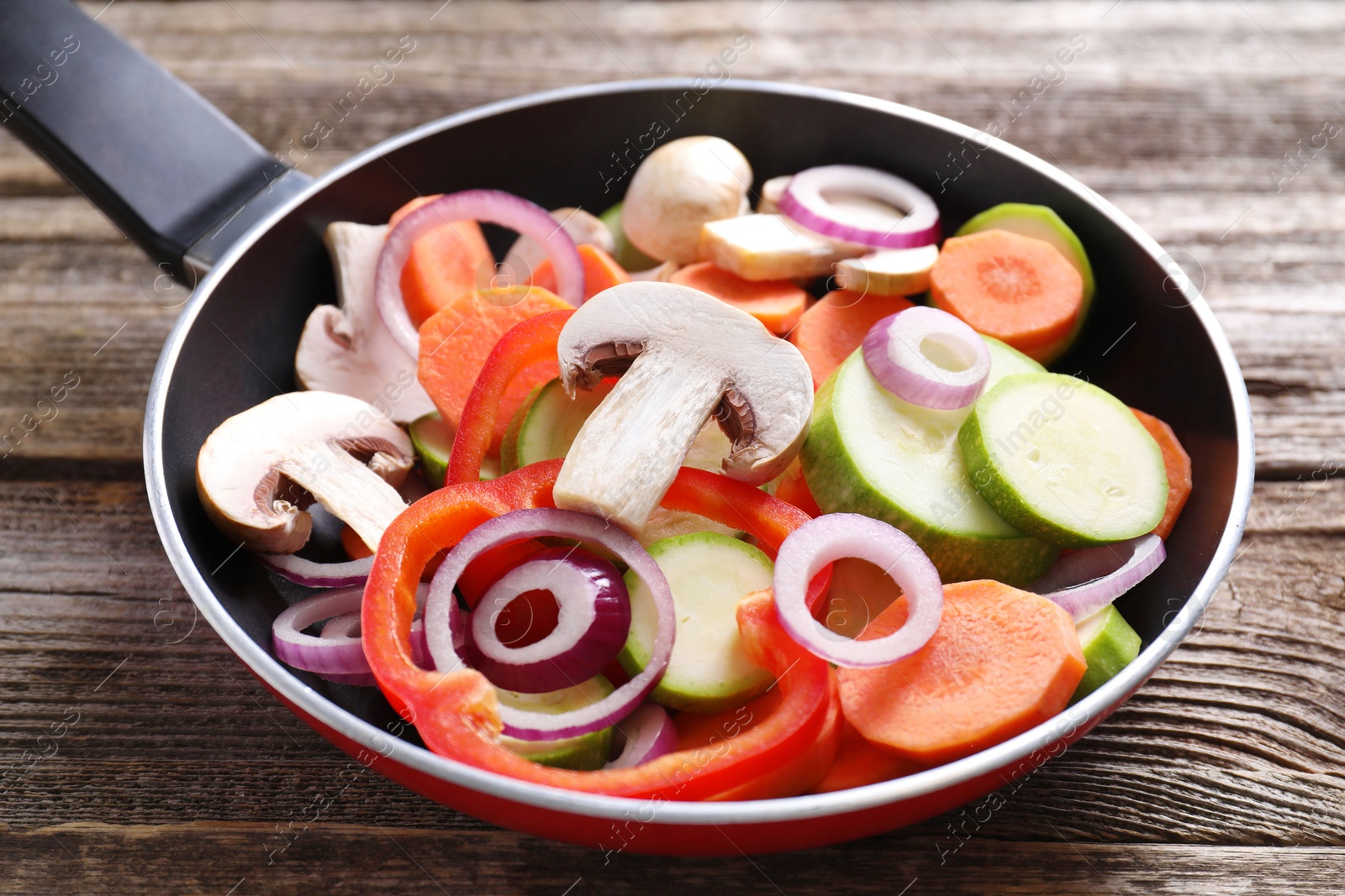 Photo of Frying pan with mix of fresh vegetables and mushrooms on wooden table, closeup