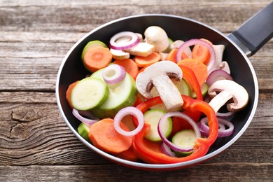 Photo of Frying pan with mix of fresh vegetables and mushrooms on wooden table, closeup