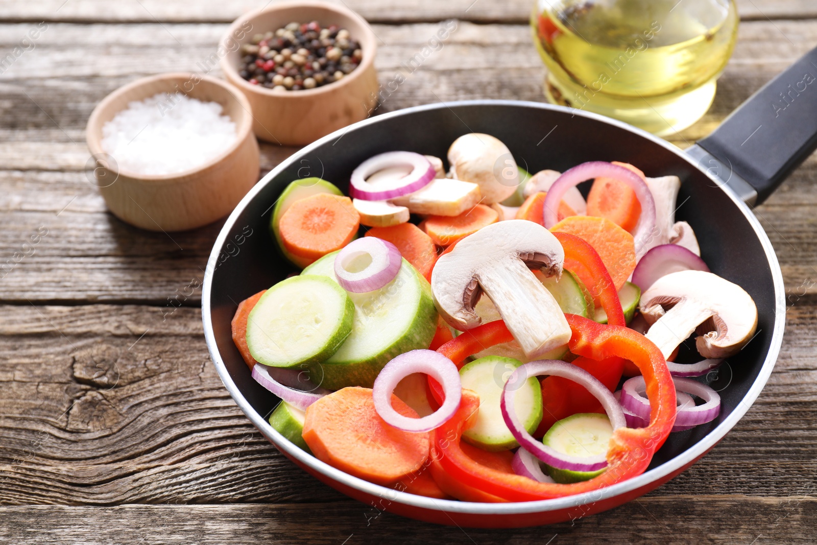 Photo of Frying pan with mix of fresh vegetables, mushrooms and spices on wooden table, closeup