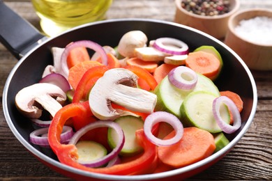 Photo of Frying pan with mix of fresh vegetables and mushrooms on wooden table, closeup