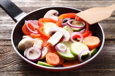 Photo of Frying pan with mix of fresh vegetables and mushrooms on wooden table, closeup