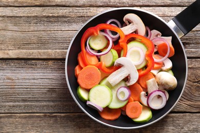 Photo of Frying pan with mix of fresh vegetables and mushrooms on wooden table, top view