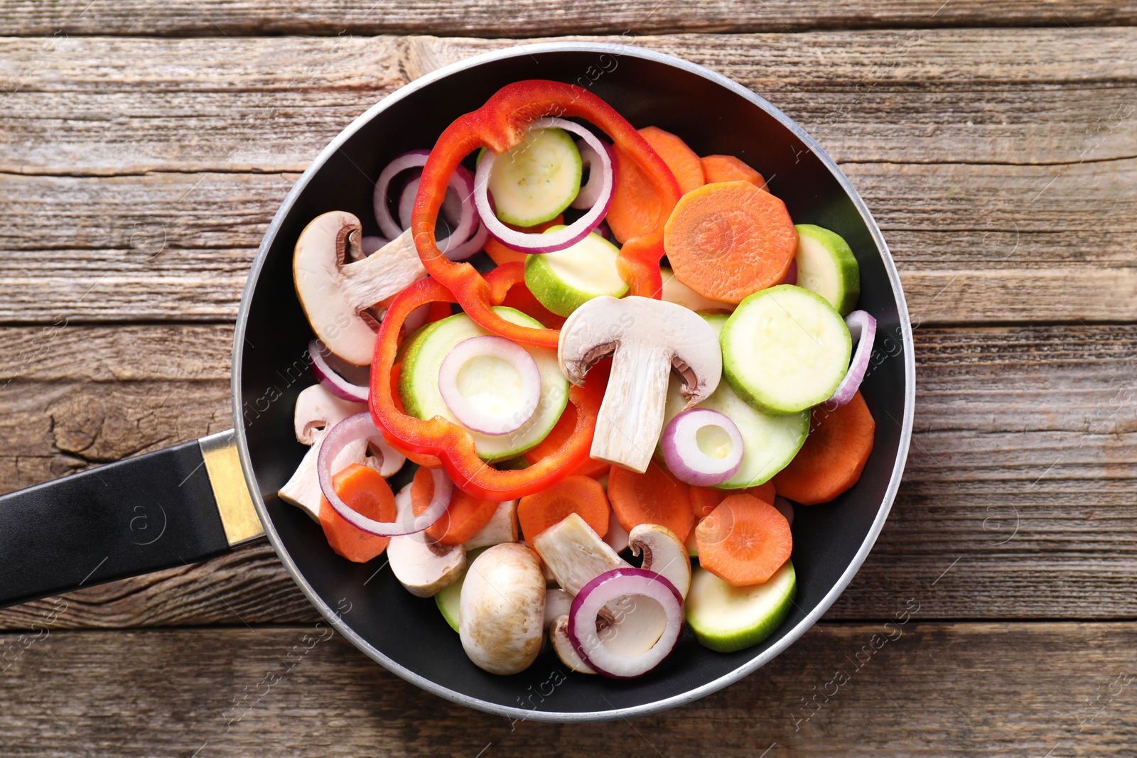 Photo of Frying pan with mix of fresh vegetables and mushrooms on wooden table, top view