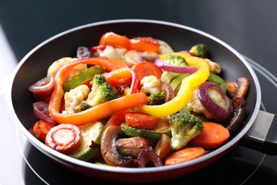 Photo of Frying pan with mix of vegetables and mushrooms on cooktop, closeup