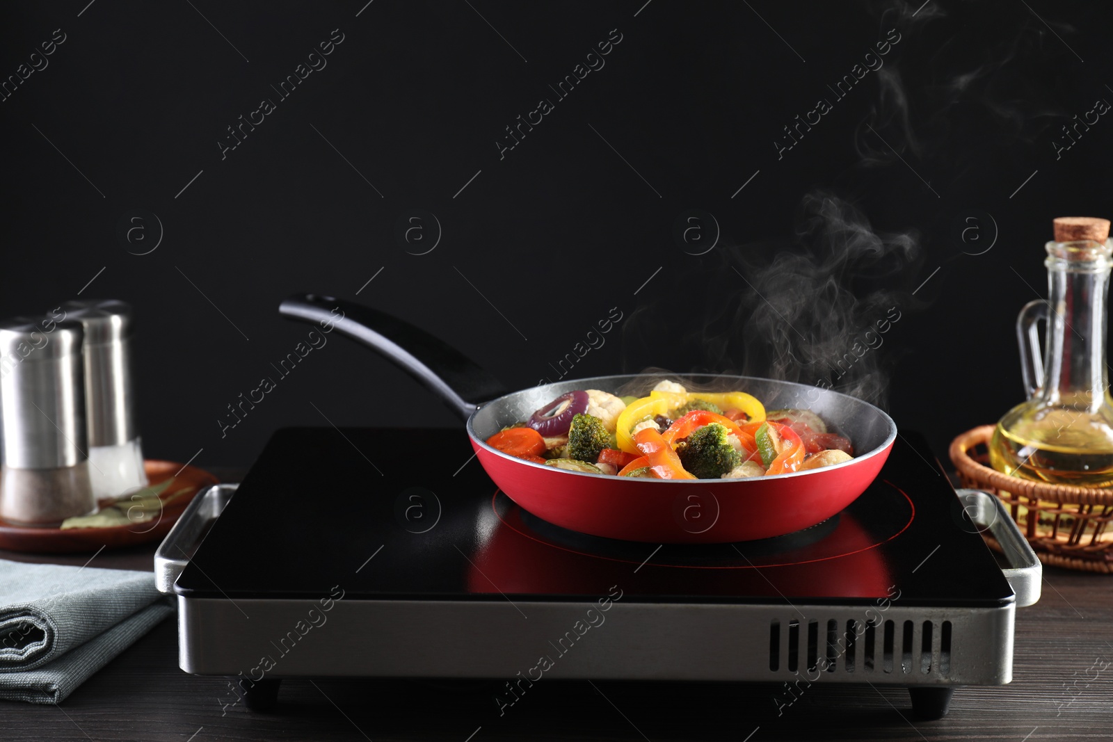 Photo of Frying pan with vegetables and stove on wooden table against black background