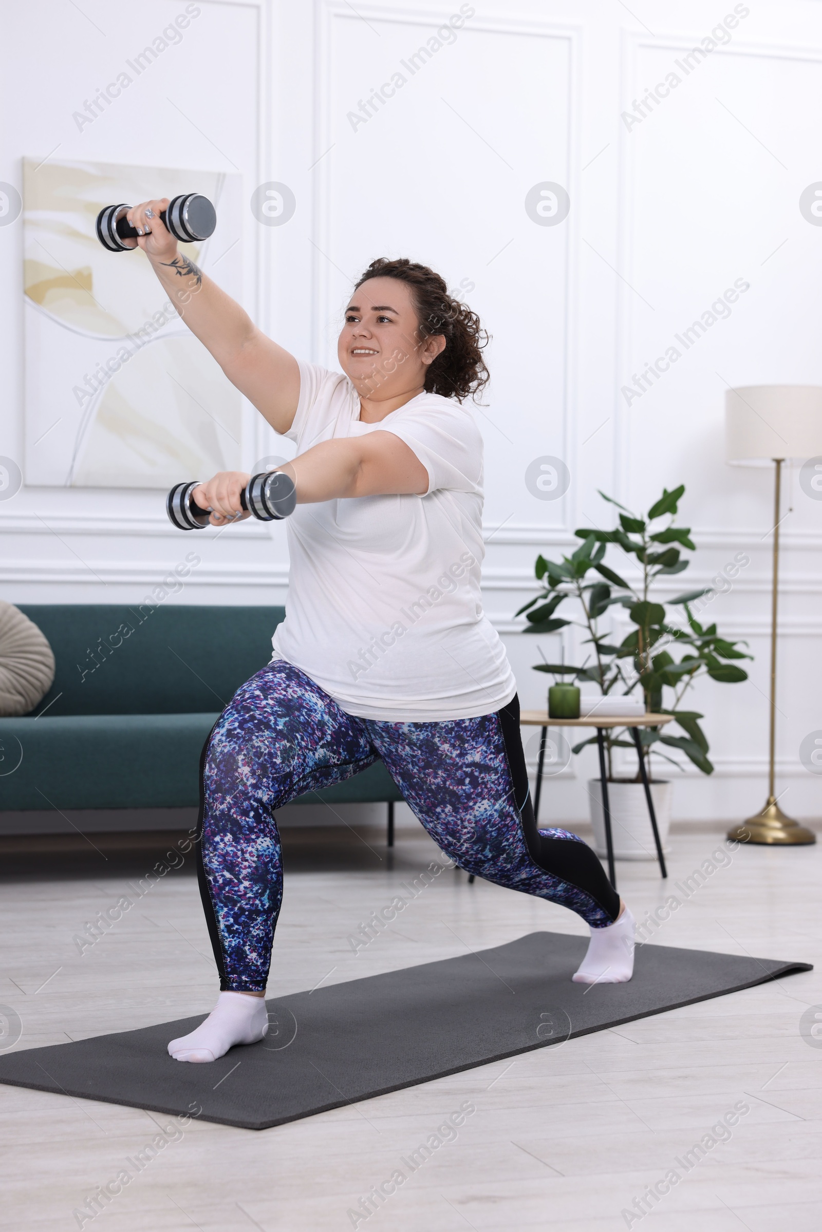 Photo of Plus size woman with dumbbells training at home