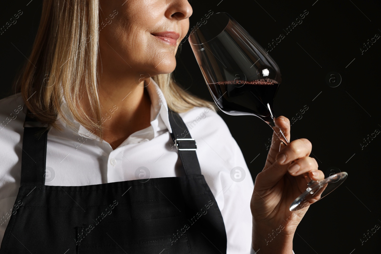 Photo of Professional sommelier tasting red wine in glass on black background, closeup