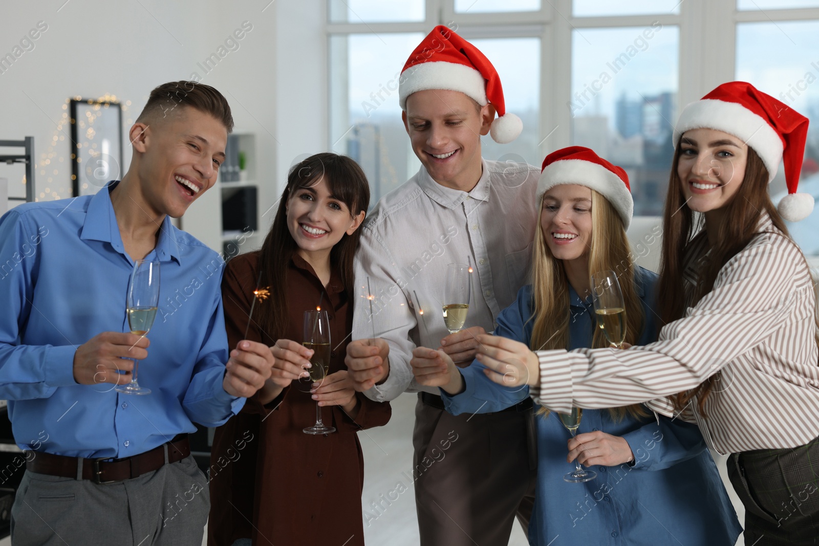 Photo of Happy colleagues with sparklers and glasses of wine at Christmas party in office