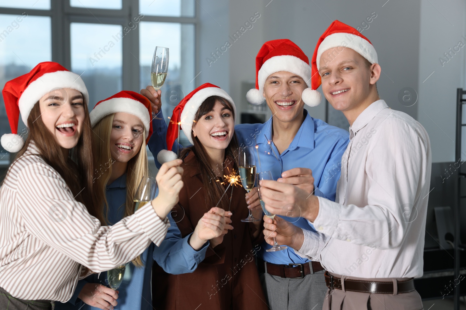 Photo of Happy colleagues with sparklers and glasses of wine at Christmas party in office