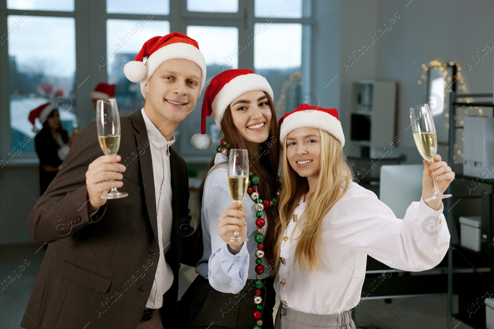 Photo of Cheerful coworkers in Santa hats with glasses of wine at office Christmas party