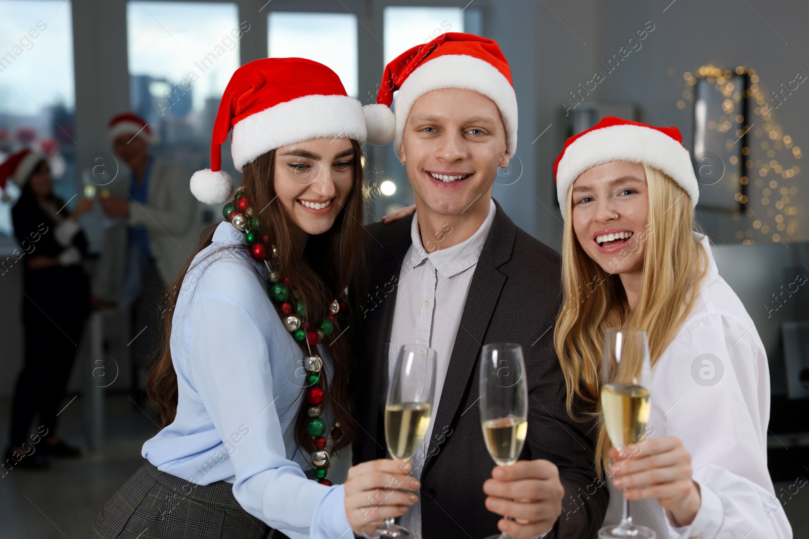 Photo of Cheerful coworkers in Santa hats with glasses of wine at office Christmas party