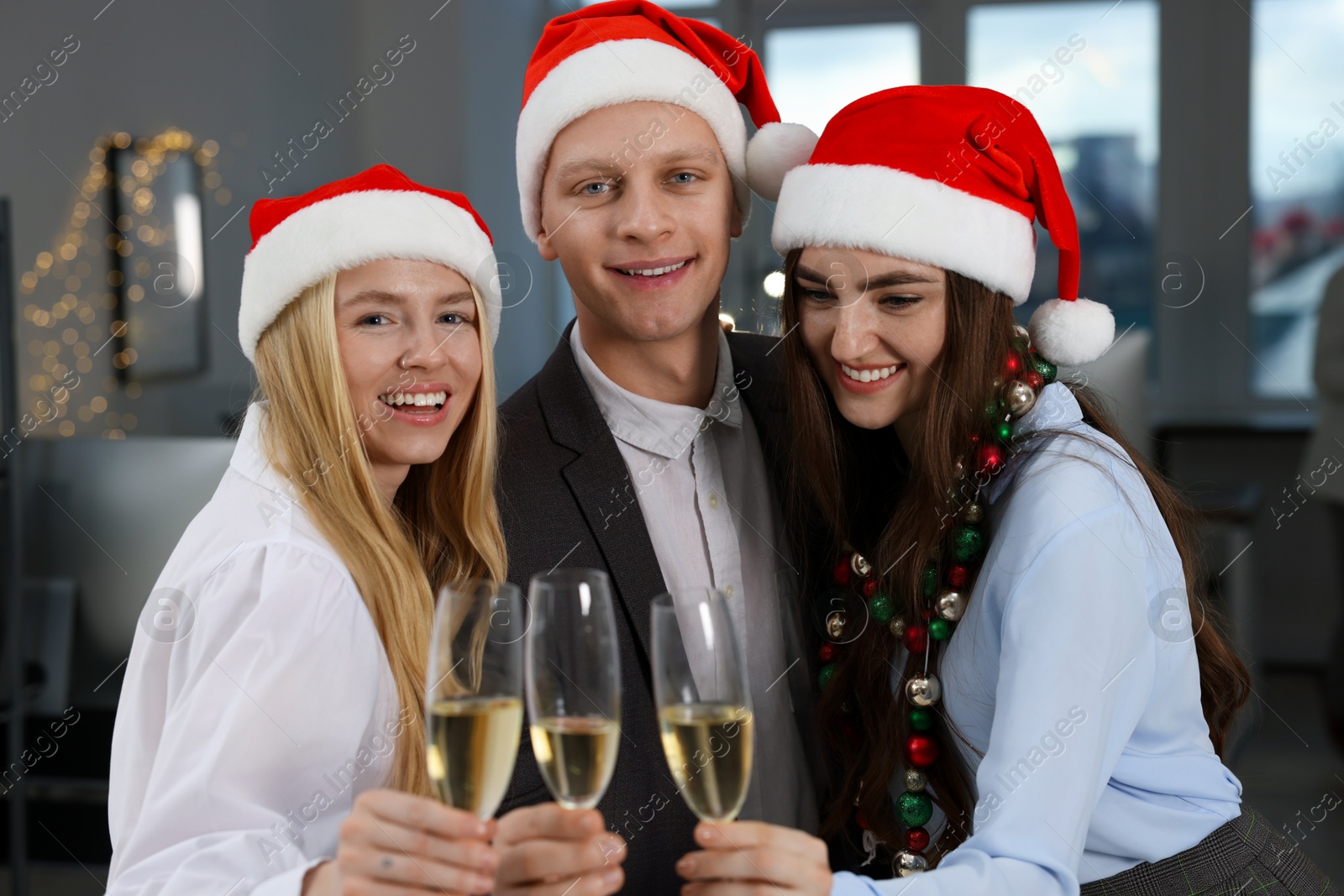 Photo of Cheerful coworkers in Santa hats with glasses of wine at office Christmas party