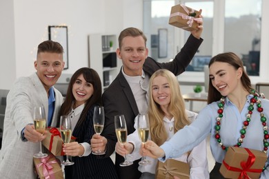 Photo of Cheerful coworkers with gifts and glasses of wine at Christmas party in office