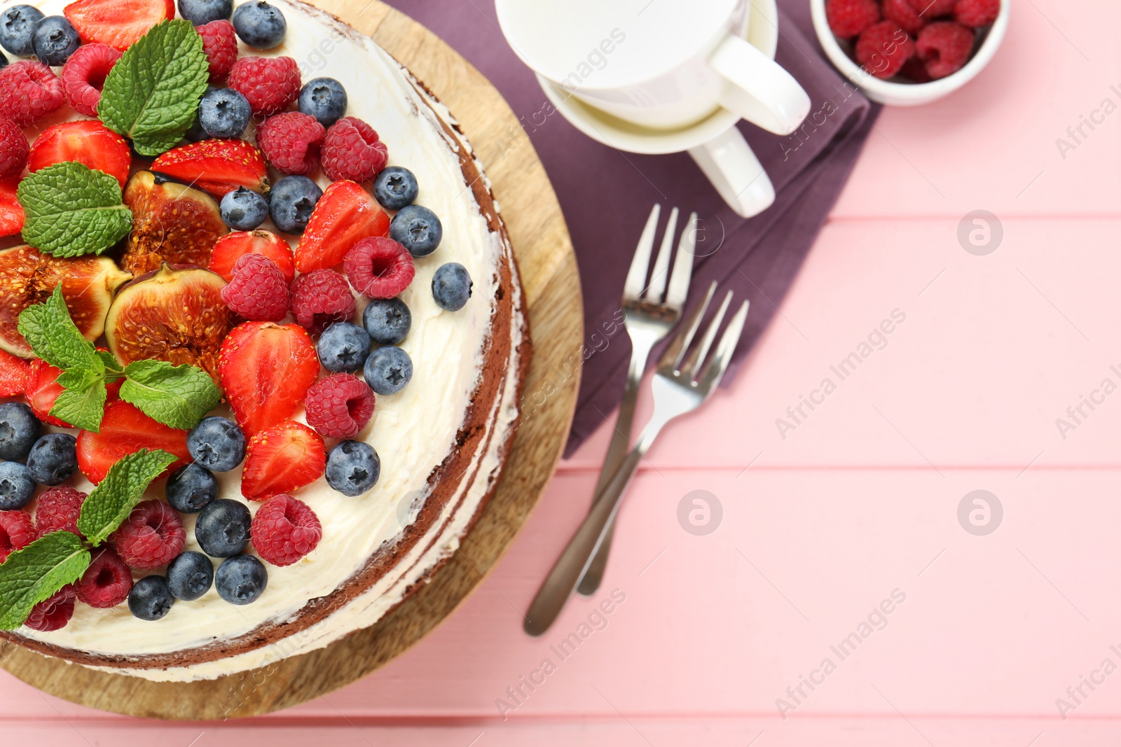 Photo of Delicious chocolate sponge cake with berries served on pink wooden table, top view. Space for text