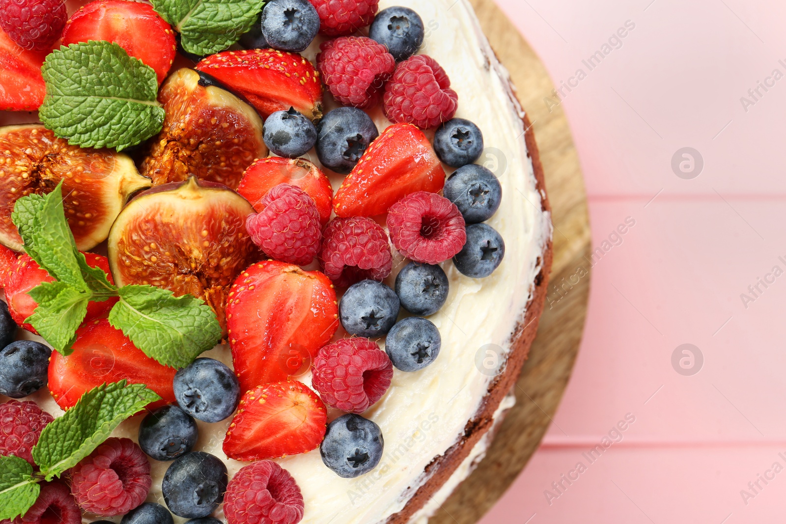 Photo of Delicious chocolate sponge cake with berries on pink wooden table, top view