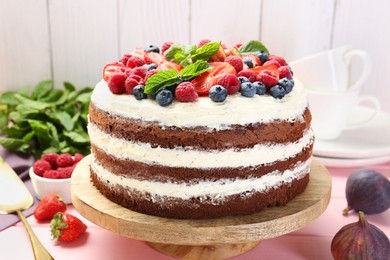 Photo of Delicious chocolate sponge cake with berries and mint on pink wooden table, closeup