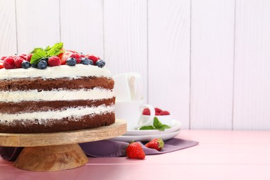 Photo of Delicious chocolate sponge cake with berries served on pink wooden table. Space for text