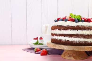 Photo of Delicious chocolate sponge cake with berries served on pink wooden table. Space for text