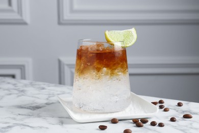 Photo of Refreshing espresso tonic drink with slice of lime and coffee beans on white marble table