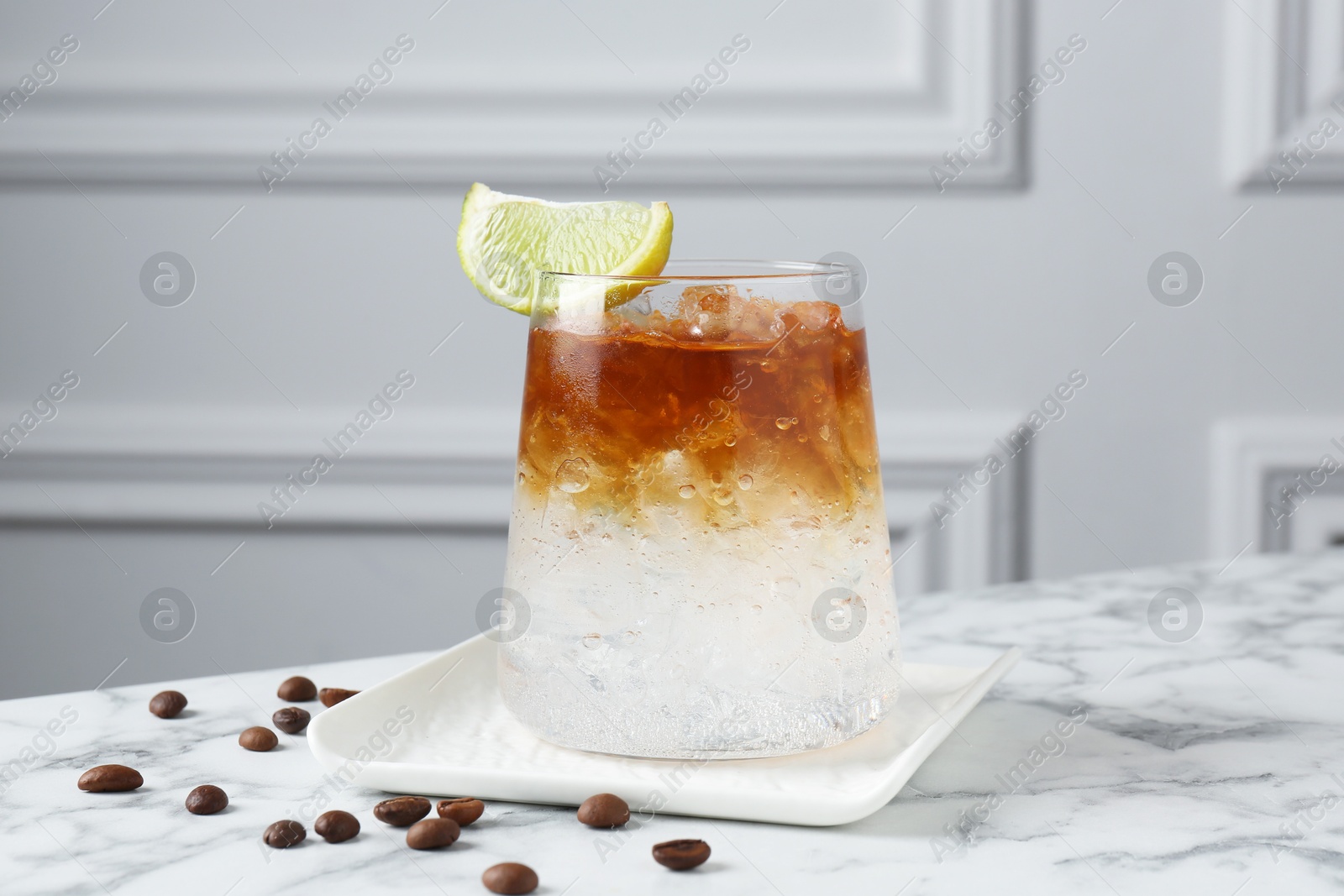 Photo of Refreshing espresso tonic drink with slice of lime and coffee beans on white marble table