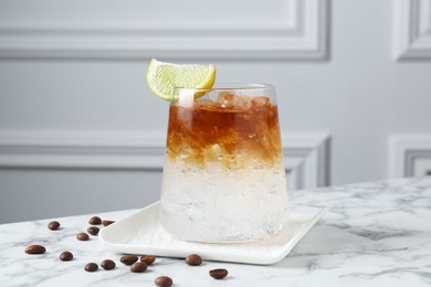 Refreshing espresso tonic drink with slice of lime and coffee beans on white marble table