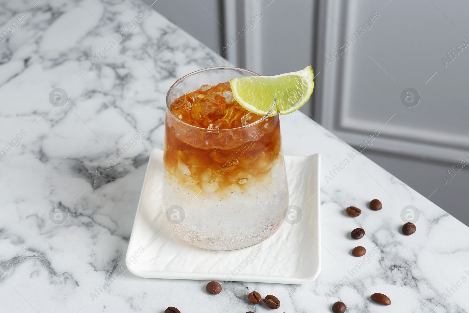 Photo of Refreshing espresso tonic drink with slice of lime and coffee beans on white marble table