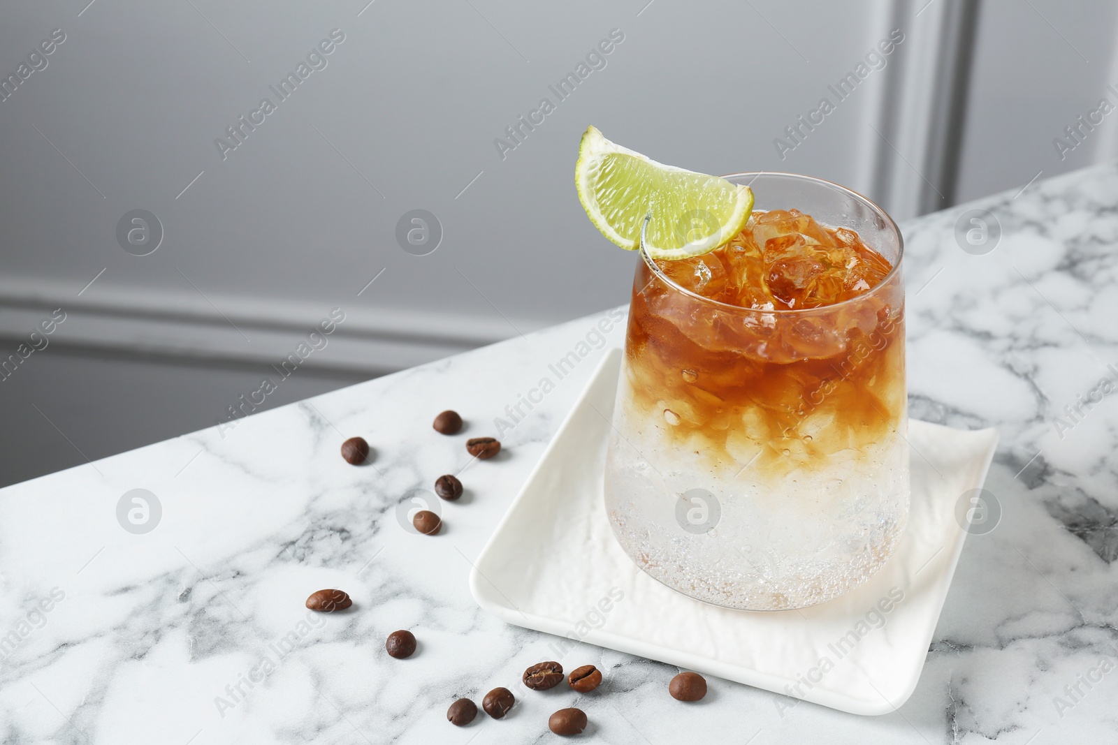 Photo of Refreshing espresso tonic drink with slice of lime and coffee beans on white marble table