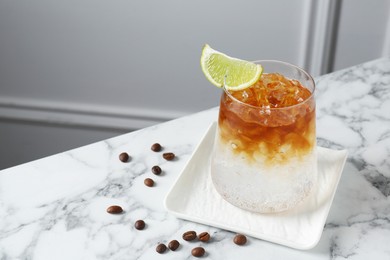 Photo of Refreshing espresso tonic drink with slice of lime and coffee beans on white marble table