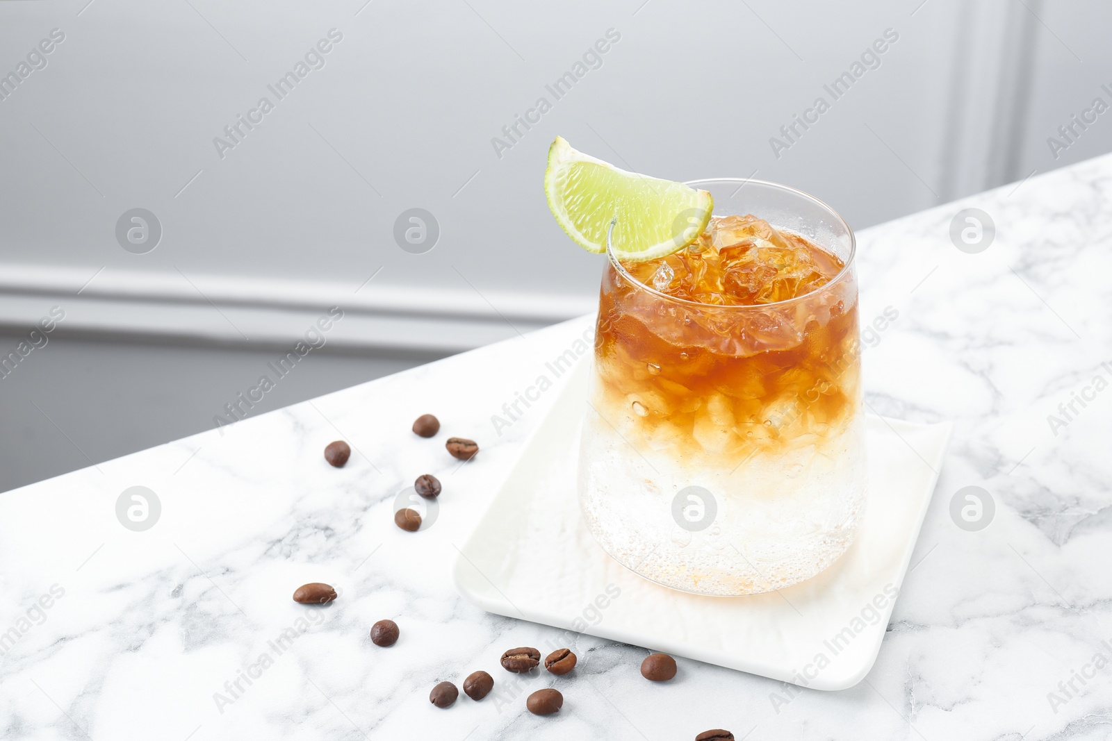 Photo of Refreshing espresso tonic drink with slice of lime and coffee beans on white marble table