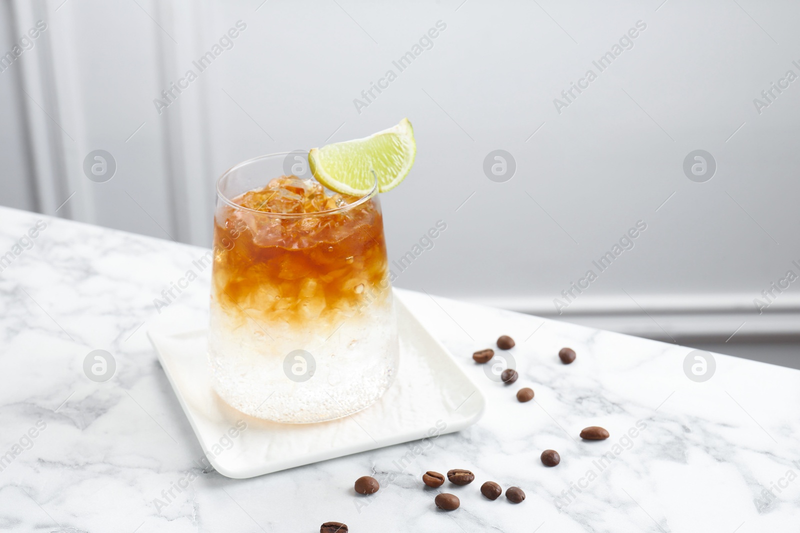 Photo of Refreshing espresso tonic drink with slice of lime and coffee beans on white marble table