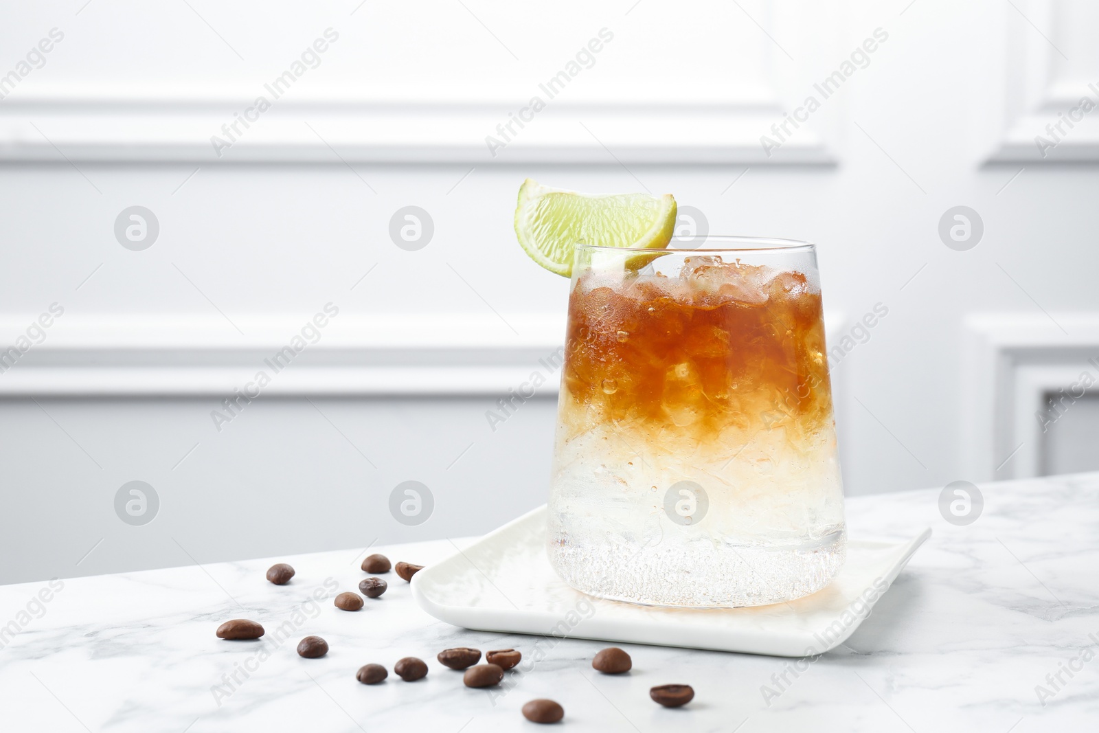 Photo of Refreshing espresso tonic drink with slice of lime and coffee beans on white marble table