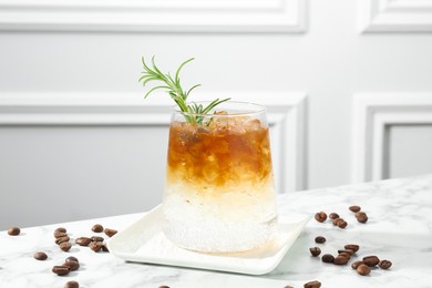 Photo of Refreshing espresso tonic drink with rosemary and coffee beans on white marble table