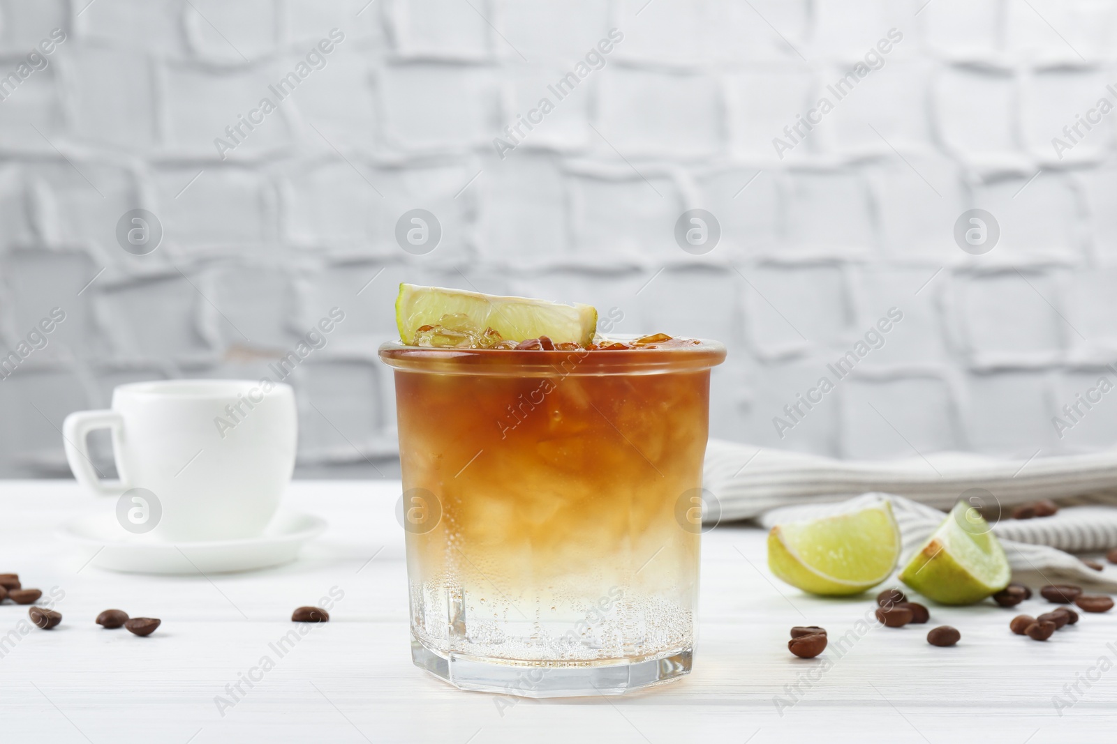 Photo of Refreshing espresso tonic drink with slice of lime and coffee beans on white wooden table