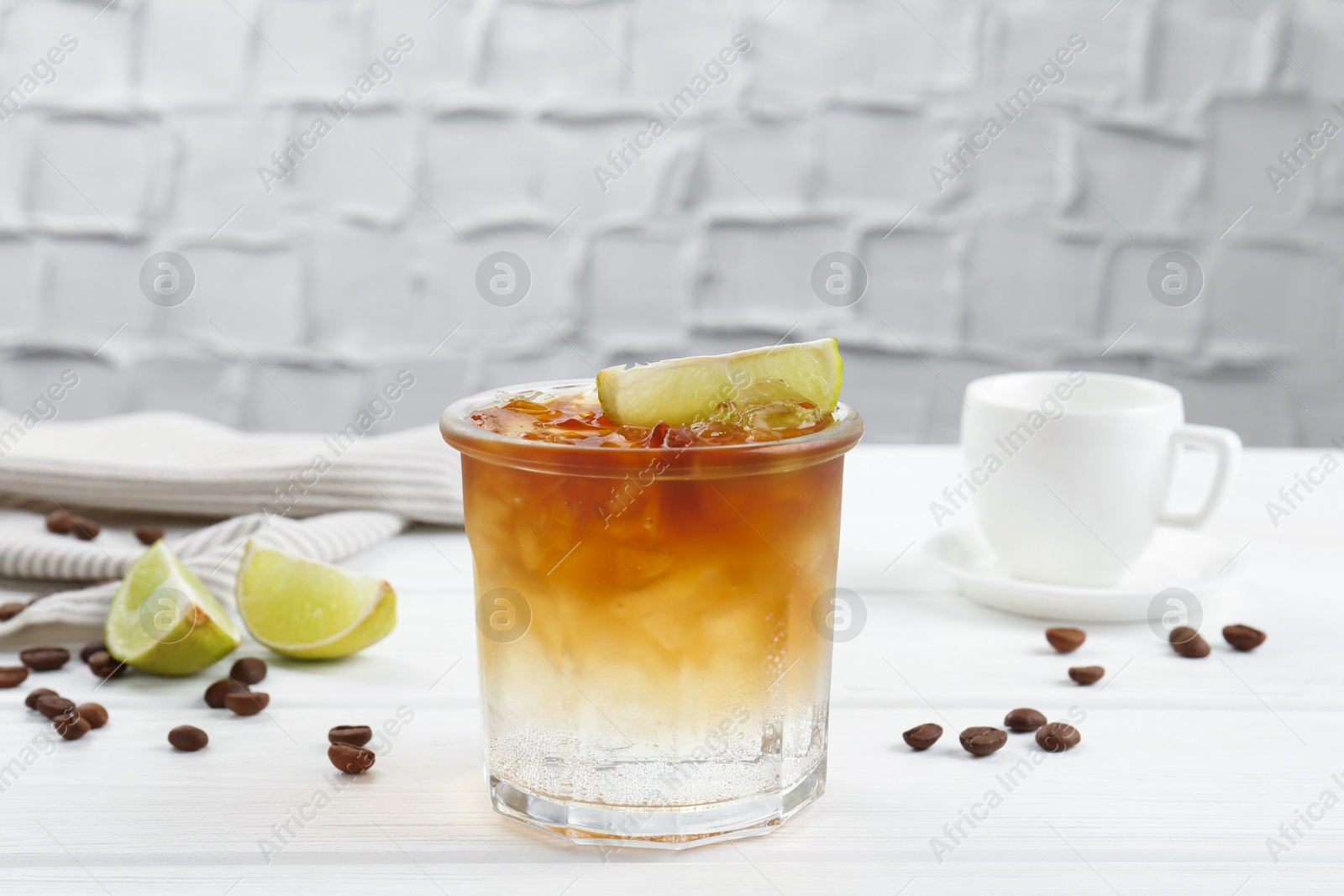 Photo of Refreshing espresso tonic drink with slice of lime and coffee beans on white wooden table