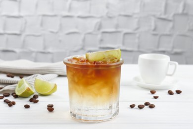 Photo of Refreshing espresso tonic drink with slice of lime and coffee beans on white wooden table